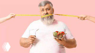 Мужчина с салатом в руке и сантиметровой лентой у шеи на розовом фоне — иллюстрация истории о похудении врача.