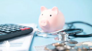 Копилка в виде свинки на светлом столе, рядом стетоскоп и калькулятор: символизируют расходы и финансовые аспекты медицины в контексте медицинских ошибок и лечения.