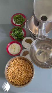 Подготовленные ингредиенты для фалафеля: сушёный нут в миске, зелень (петрушка/кинза), чеснок и специи на кухонном столе рядом с блендером