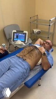 Врач лежит на кушетке в кабинете; на живот приложены датчики аппарата iLivtouch для фиброэластометрии; на мониторе виден результат.