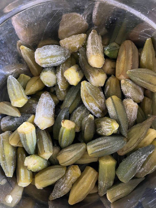 Молодые стручки бамии в металлической миске — зелёные, свежие, длиной около 2–10 см; видны ребристые поверхности, срезы и капли влаги.