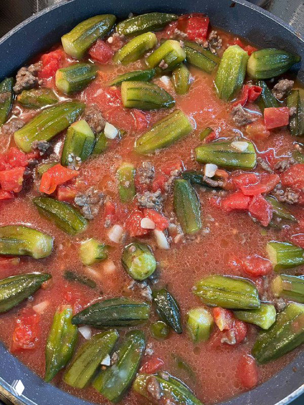 Бамия с томатами в сковороде: стручки плавают в густом томатном соусе с кусочками помидоров, соус начинает густеть и обволакивать овощи.