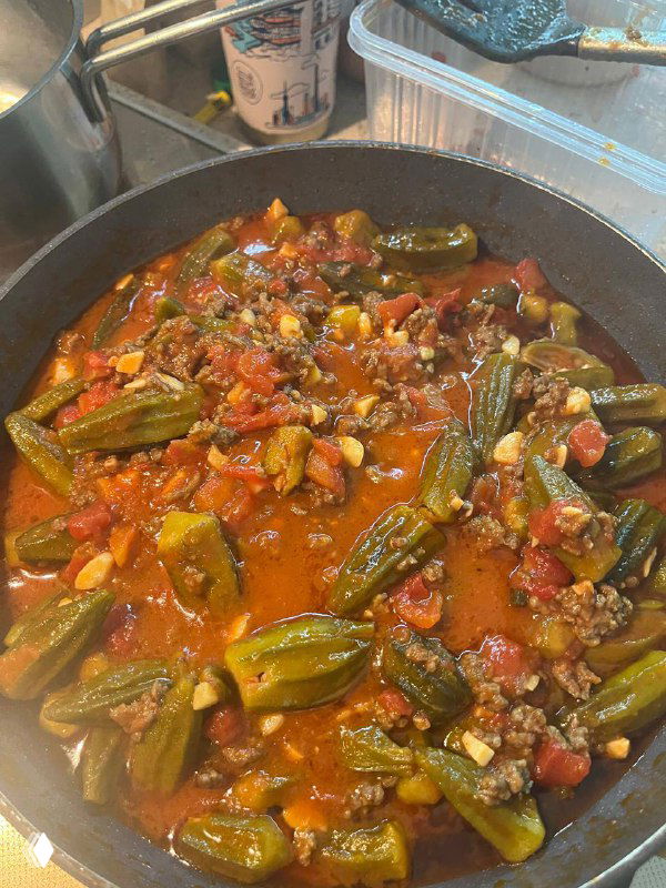 Готовое блюдо бамия с томатным соусом и фаршем в сковороде — насыщенный соус, равномерно покрывающий стручки, видна готовность к подаче.