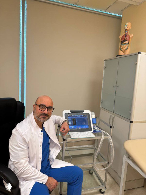 Врач в белом халате рядом с аппаратом iLivtouch FT 100 в кабинете; видна консоль прибора и медицинская мебель в клинике.