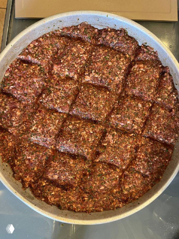 Противень с запечённым фаршем «лахме биль синия», поверхность разрезана на порции; видна румяная корочка и крошки овощей.