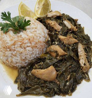 Тарелка млюхии с кусочками курицы и густой зелёной подливкой рядом с белым рисом и дольками лимона — домашний восточный обед.