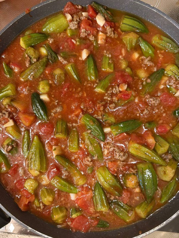 Вид сверху: сковорода с тушёной бамией в томатном соусе с говяжьим фаршем и кусочками помидоров, готовое домашнее блюдо для семьи