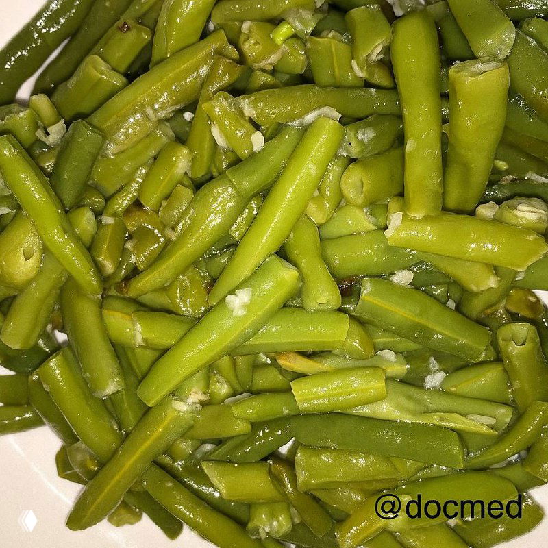 Тарелка тушёной стручковой зелёной фасоли с кусочками чеснока и блеском оливкового масла — крупный план.