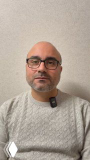 Портрет врача-гастроэнтеролога в светлом свитере и в очках, на груди закреплён небольшой микрофон; нейтральная стена на фоне, снимок для видео о изжоге.