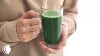 Руки держат прозрачный стакан с ярко‑зелёным напитком (хлорофилл); изображение иллюстрирует тему добавок и влияние на ЖКТ.