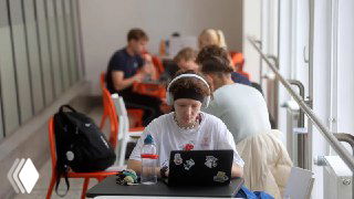 Человек за ноутбуком в коворкинге, ноутбук с наклейками, другие люди на фоне — иллюстрация работы цифрового кочевника.