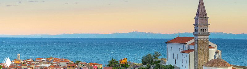 Панорамный вид прибрежного словенского города с морем, крышами домов и колокольней; иллюстрация к посту о ВНЖ для диджитал-номадов.