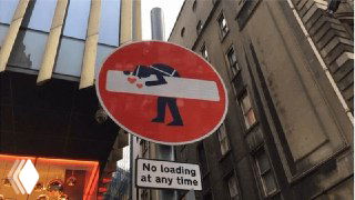 Фотография дорожного знака 'въезд запрещён' с изображением человека, наклоняющегося через белую полосу на городской улице