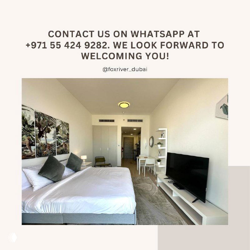 Close interior shot of the furnished studio showing the bed, cushions, wall art and TV stand in a clean, modern short-stay unit.