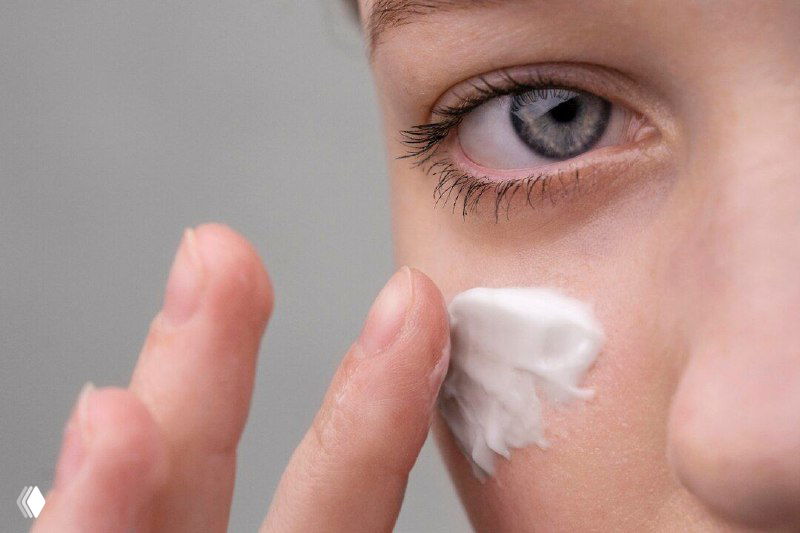 Крупный план: человек наносит крем на кожу под глазом — демонстрация ухода за лицом и использования косметического продукта в рутинной процедуре.