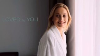 Улыбающаяся женщина в халате у окна, брендовый кадр Loved by You, передающий атмосферу уютного и бережного ухода за кожей.