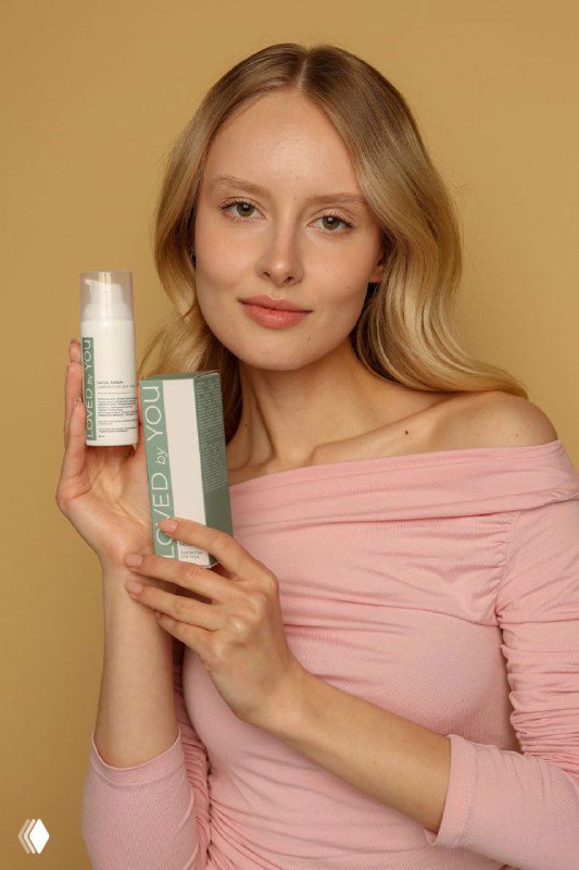 Женский портрет: модель держит флакон и коробку сыворотки Loved by You на бежевом фоне, видно оформление упаковки и бренд.