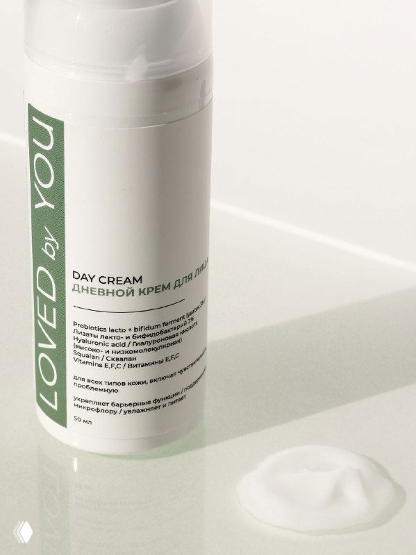 Флакон дневного крема Loved by You на светлом фоне рядом с небольшим вспененным образцом текстуры крема.