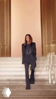 Женщина в тёмном деловом костюме спускается по светлой мраморной лестнице в элегантном интерьере — образ люксового бренда и стиля.