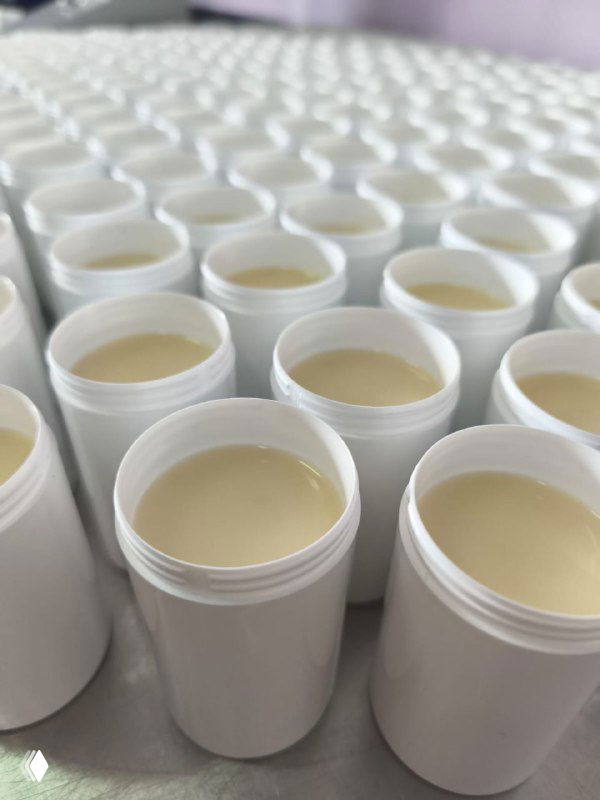 Ряды открытых белых баночек с кремом на производственном столе, показывающие текстуру, объём и стадию фасовки косметической продукции.