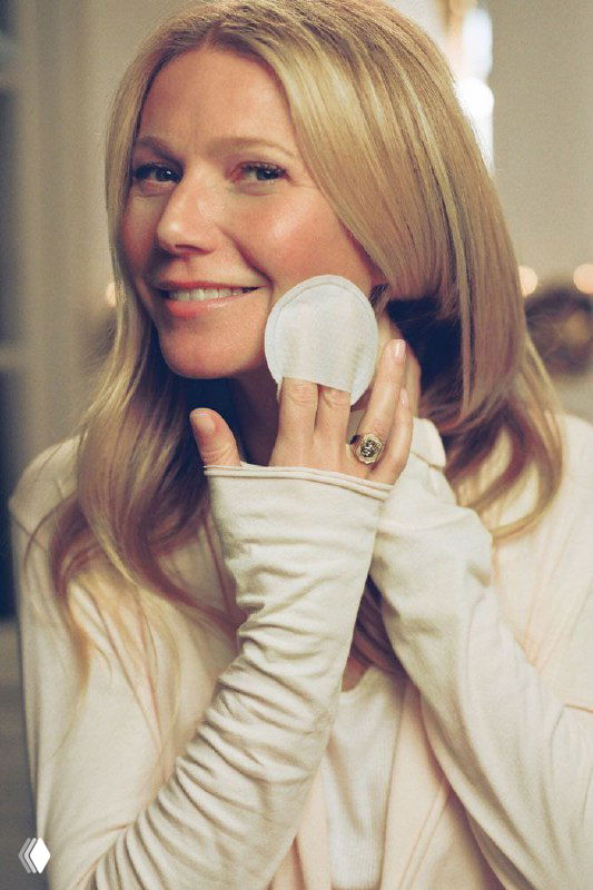 Женщина в светлом свитере держит ватный диск у лица, иллюстрируя уход за кожей и идею поддержки её микробиома.