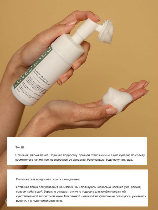 Рука выдавливает мягкую пену из флакона пенки для умывания Loved by You; видно текстуру пены и упаковку на бежевом фоне.