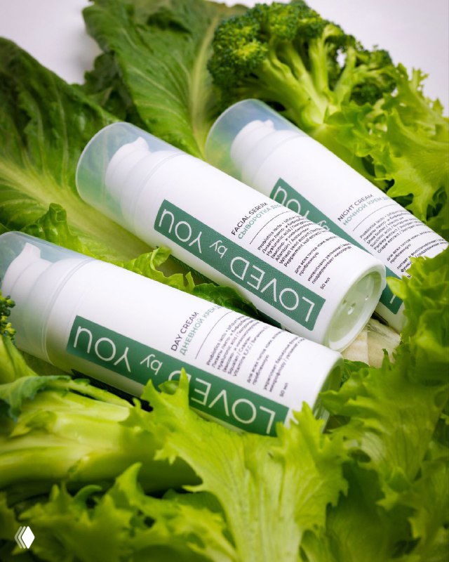 Флаконы косметики Loved by You, размещённые на зелёных листьях, показывают упаковку бренда и ассоциацию с натуральностью и микробиомной заботой.