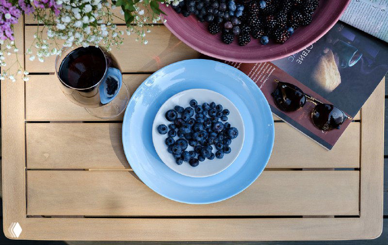 Крупный план столешницы с тарелкой черники и чашкой кофе на деревянном столике — детализация сервировки на террасе.
