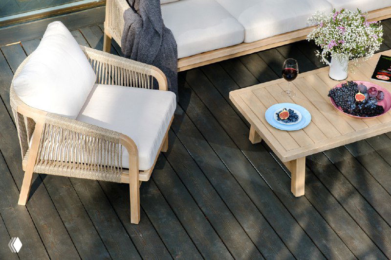 Кресло и низкий стол из той же коллекции: бежевые подушки, деревянная структура и кухонная посуда на столе.