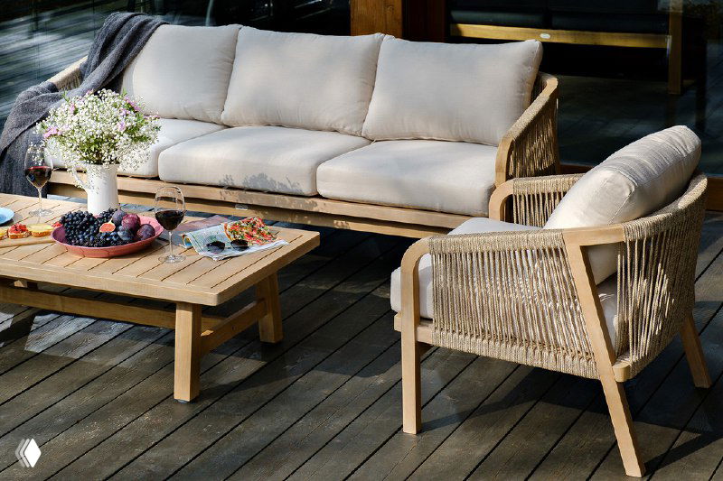 Общий вид на светлый диван и кресло RIMINI с низким столиком, сервировка и декоративные элементы на террасной доске.