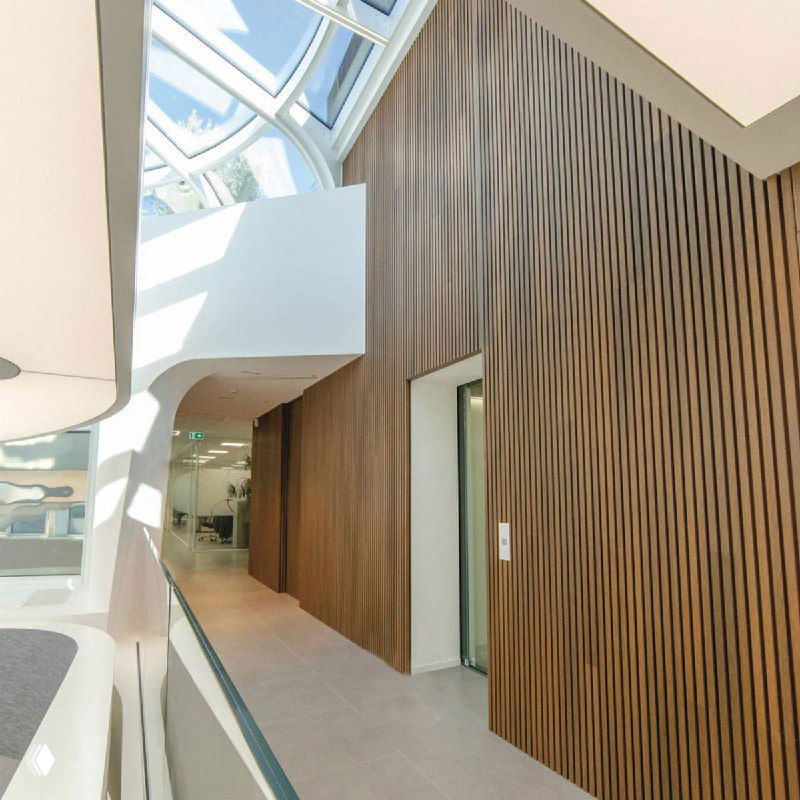 Интерьерное фото с высоким коридором и стеной, облицованной вертикальными брусковыми панелями из ДПК тёмно-коричневого оттенка, демонстрирующее масштаб и дизайн.