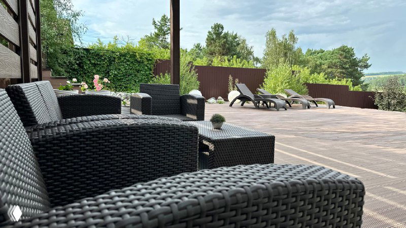 Крупный план комплектной пластиковой мебели ротанг‑стиля на террасе, кресла и столик рядом с зоной отдыха и панорамным видом.