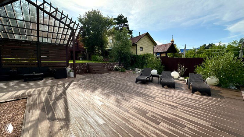 Панорамный вид на просторную террасу с расставленными шезлонгами и зелёной оградой участка, светлая атмосфера загородного отдыха.