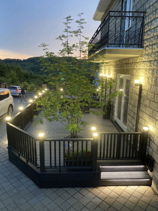 Чёрная терраса вечером с подсветкой вдоль перил и настила, вид с угла демонстрирует атмосферу и равномерность освещения на площадке.