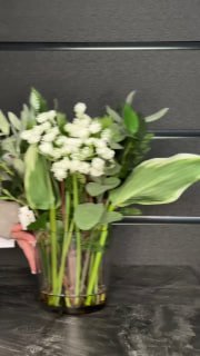 Букет белых цветов с зеленью в прозрачной вазе на тёмном столе — демонстрация флористической композиции и декора магазина.