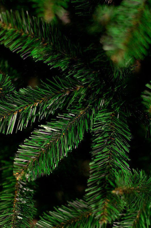 Фрагмент ветки искусственной ёлки в крупном плане: блеск пластика и форма иголок ПВХ видны при сравнении с литой версией.