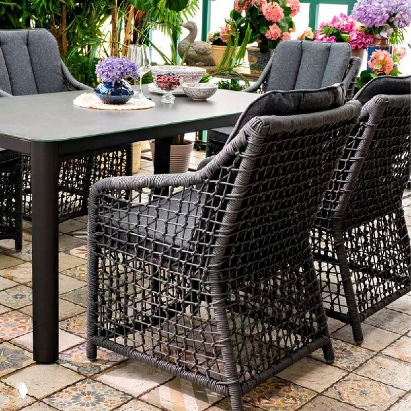 Крупный план набора LUCCA: тёмный стол и кресла с плетёными спинками, декоративные элементы и цветы на столе; вид сбоку для демонстрации дизайна.