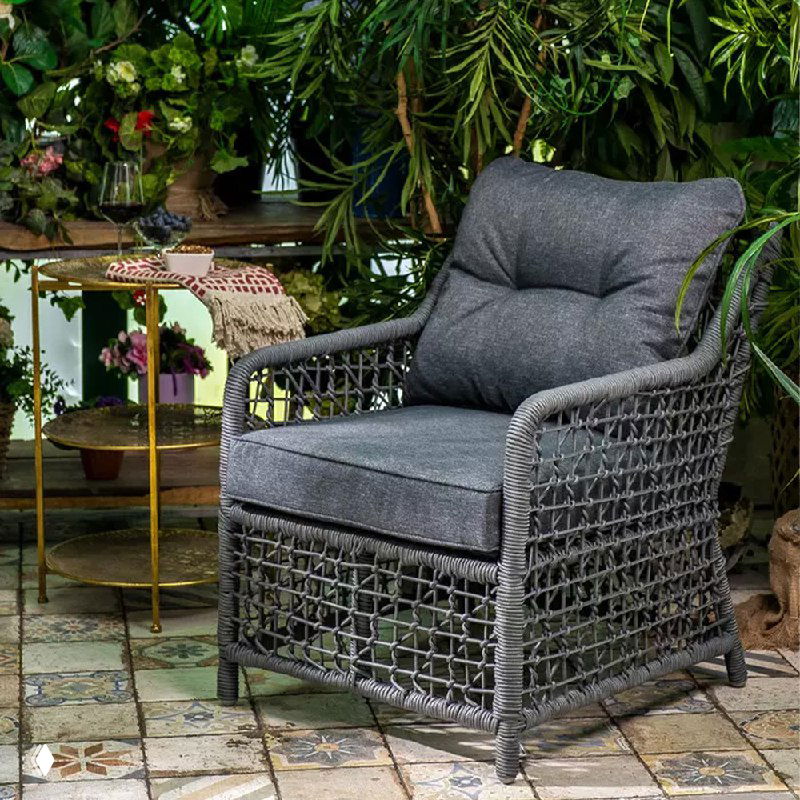 Удобное кресло LUCCA с большой мягкой подушкой на террасе: плетёная рама, тёмная обивка и растительный фон для уютной атмосферы.