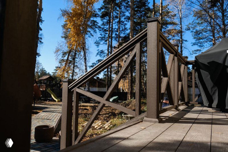 Угол террасы с декоративным ограждением из ДПК, крупный план пандуса и осенние деревья на заднем плане, чистая укладка.