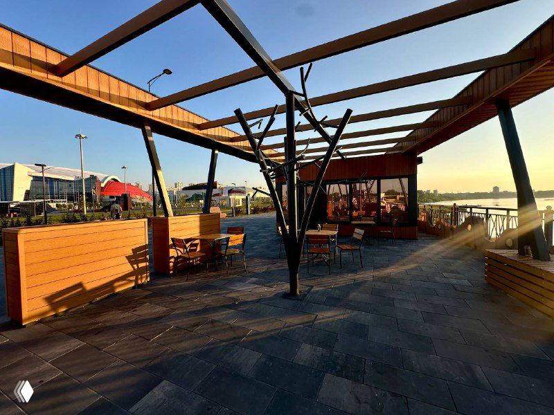 Широкий вид на модульную зону с террасой и столиками: покрытие из ДПК, вечерний свет и пространство для прогулок и отдыха у воды.