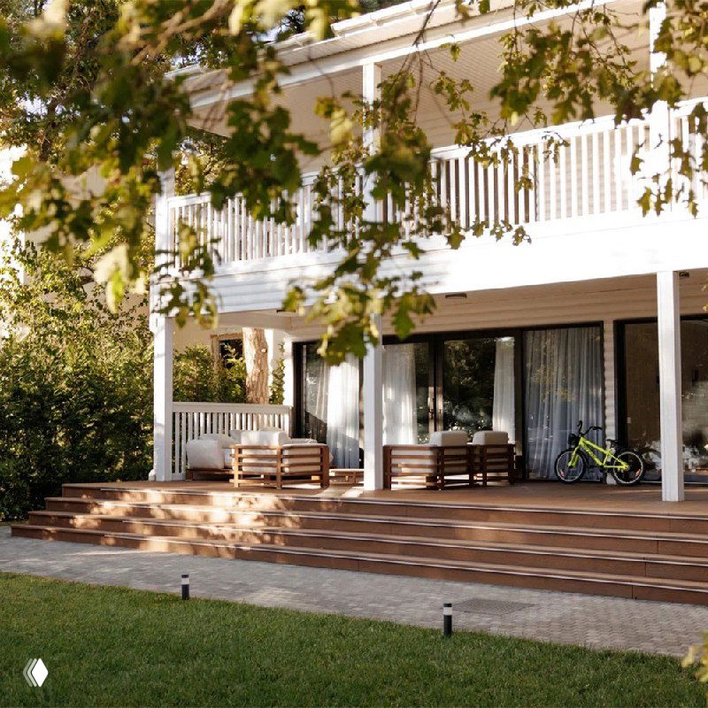 Терраса из ДПК перед домом: настил из композитной доски, садовая мебель и зелёные деревья на заднем плане