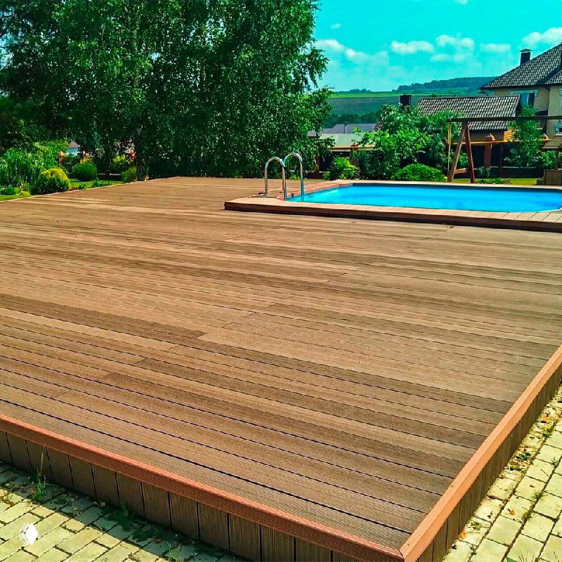 Широкая терраса из ДПК у бассейна: вид крупным планом на доски, швы между досками и ландшафтный фон с деревьями