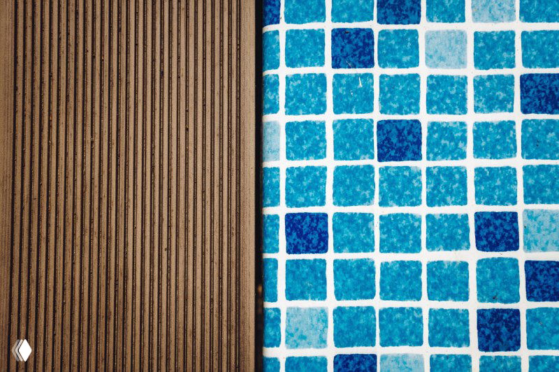Крупный план: композитная террасная доска NewWood рядом с мозаичной облицовкой бассейна — текстура доски и голубые плитки рядом.