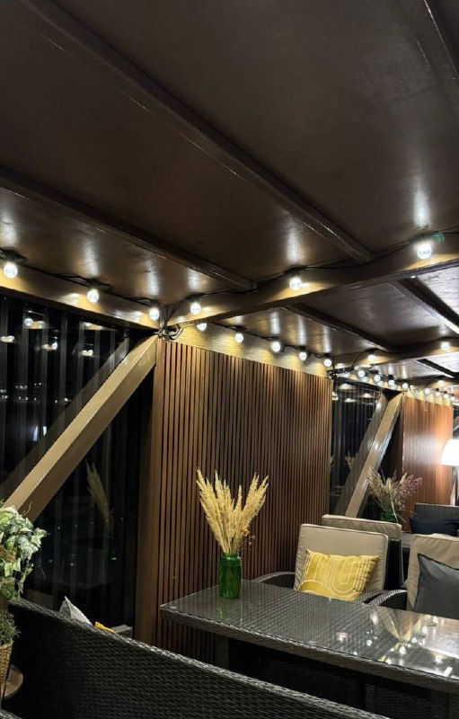 Интерьерная зона с брусковыми панелями из ДПК, тёплое освещение по верхнему карнизу, стол и декоративные сухоцветы в центре.