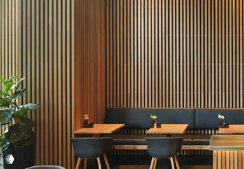 Интерьер кафе с панелями из ДПК в виде вертикальных реек, мягкие диваны и столы, акцент на текстуру и современный дизайн.