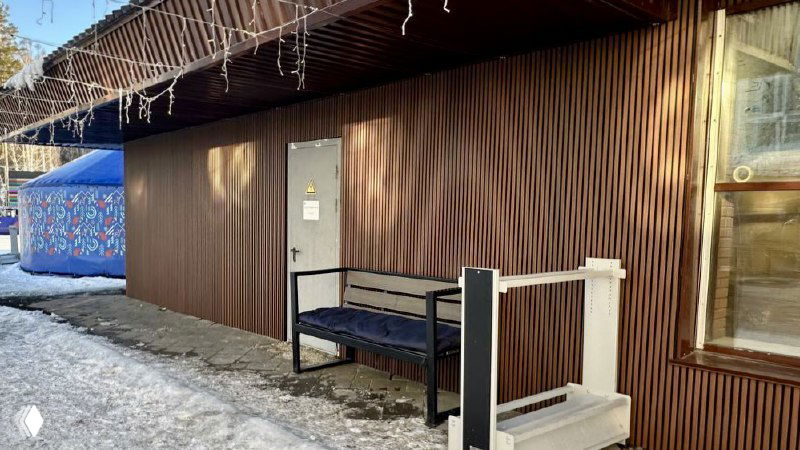 Входная часть и торец фасада ресторана «Танай», брусковые панели из ДПК, уличная скамья, ступеньки и ледяной покров на тротуаре перед зданием.