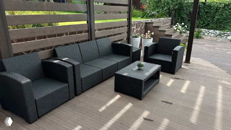 Угловая зона отдыха на террасе с мебелью из ротанга, аккуратным настилом из ДПК и декоративными растениями — демонстрация практичности покрытия.