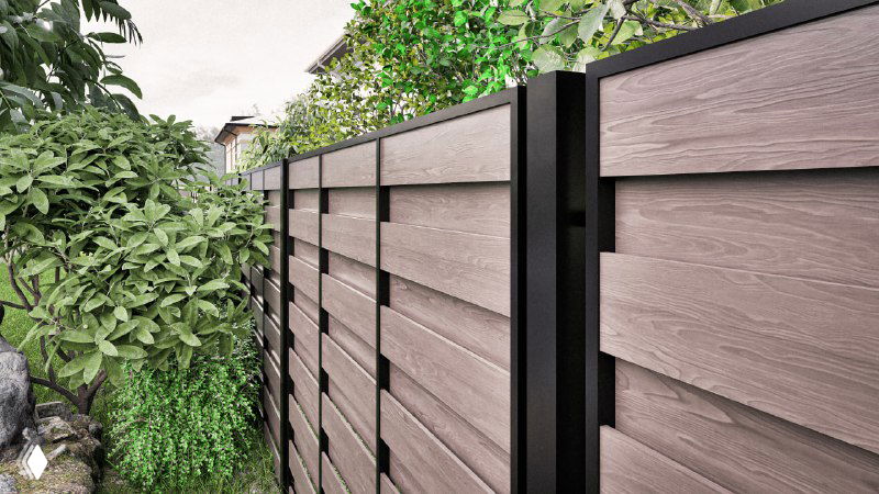 Ближний ракурс панели забора из ДПК: фактура доски, металлический профиль каркаса и растения у основания секции, вид снизу.