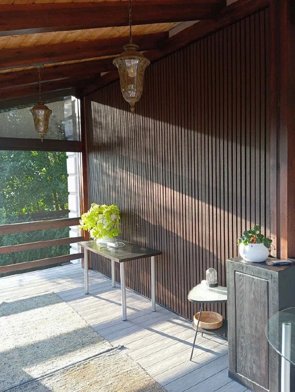 Колоритная веранда с брусковыми деревянными панелями, солнечным светом и простыми садовыми аксессуарами, ощущение природы и тепла.