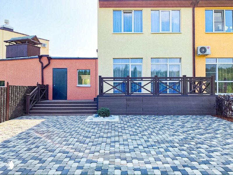 Панорамный вид участка с террасой из ДПК ProDecking у дома: ограждение, мощёная площадка, зелёные насаждения и соседние строения.